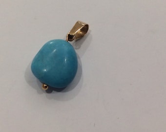 May include: A turquoise gemstone pendant with a gold bail and a small gold bead at the bottom.