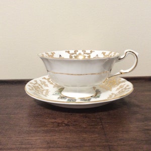 May include: A white teacup and saucer with gold trim and a floral pattern. The saucer has a gold rim and a floral design.