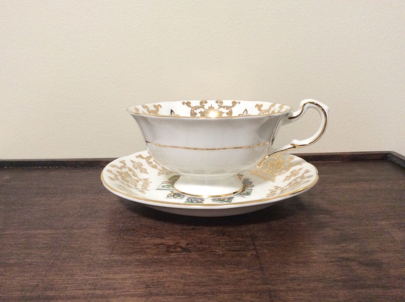 May include: A white teacup and saucer with gold trim and a floral pattern. The saucer has a gold rim and a floral design.