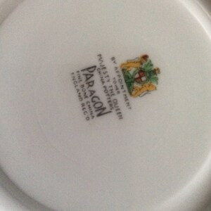 May include: White porcelain plate with a black and white logo that reads "Paragon Fine Bone China England  Reg'd" and a crest with the text "By Appointment to Her Majesty The Queen China Pottery".