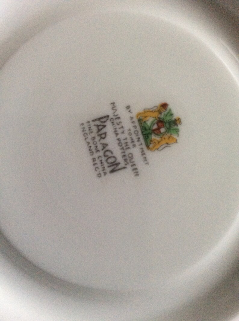 May include: White porcelain plate with a black and white logo that reads "Paragon Fine Bone China England  Reg'd" and a crest with the text "By Appointment to Her Majesty The Queen China Pottery".