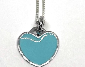 May include: A silver necklace featuring a heart-shaped pendant. The pendant has a light blue enamel centre and a silver border. The necklace chain is also silver, set against a white backdrop.