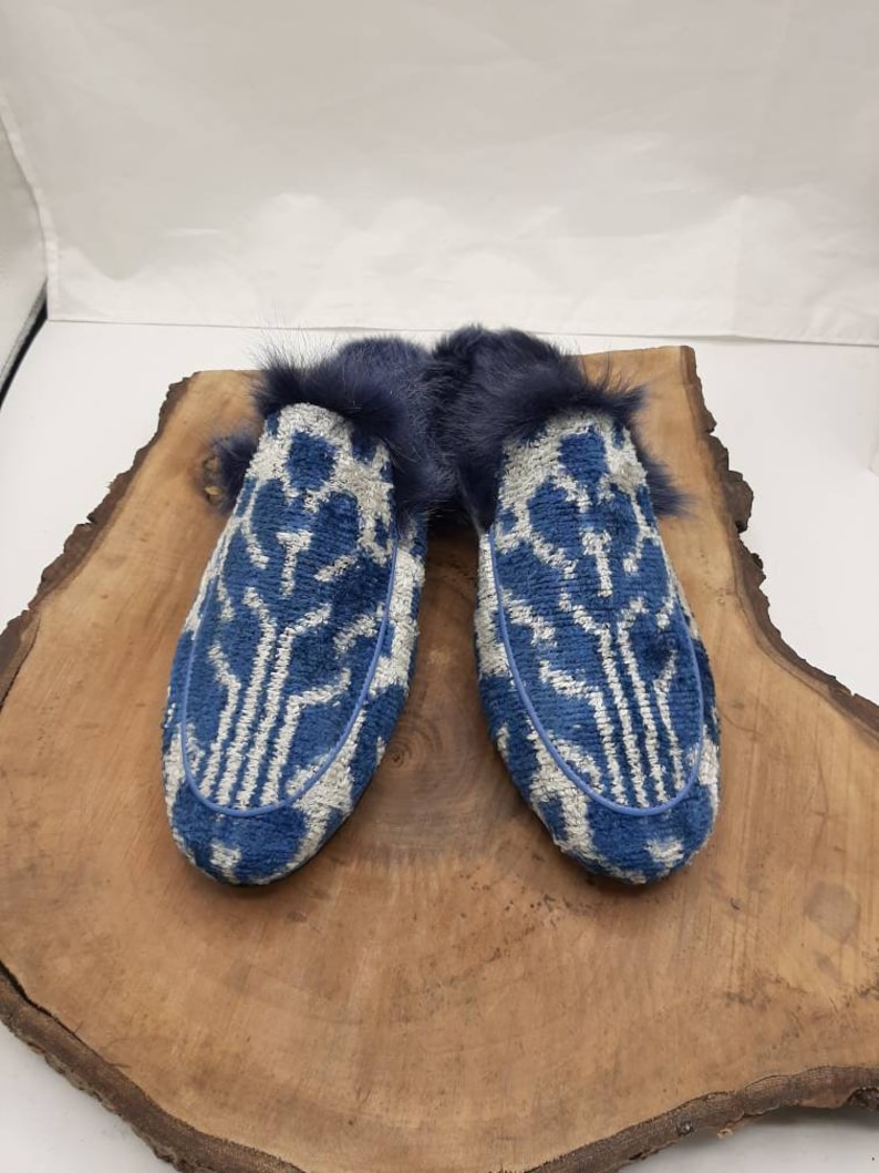 May include: A pair of blue and white patterned slippers with a faux fur lining. The slippers are on a wooden surface.