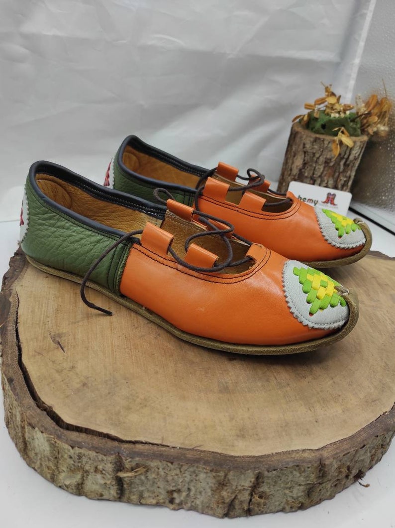 K&ouml;nnte beinhalten: Ein Paar orangefarbene und gr&uuml;ne Lederschuhe mit einem dekorativen Stichdesign an der Spitze. Die Schuhe haben Schn&uuml;rsenkel und ein braunes Lederfutter.