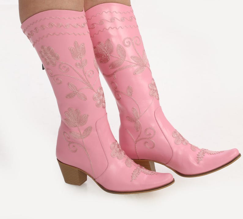 May include: A pair of pink cowboy boots with floral embroidery. The boots have a pointed toe and a block heel.