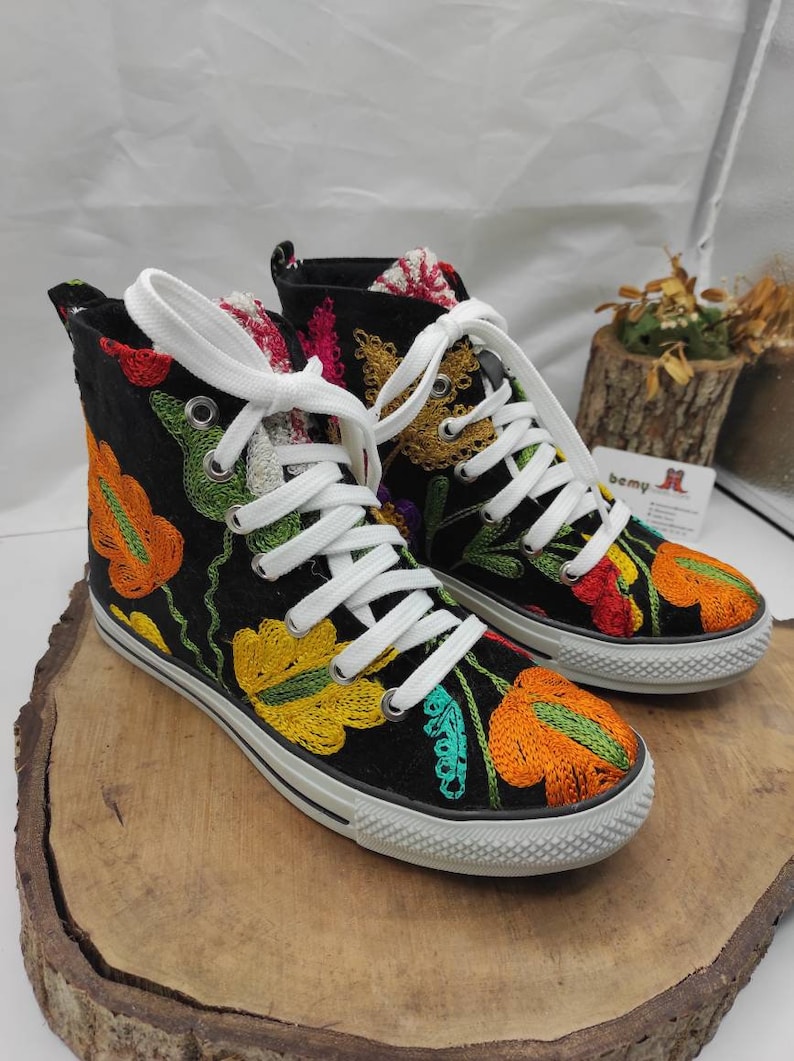 May include: Black high-top canvas shoes with colorful floral embroidery. The shoes have white laces and a white rubber sole.