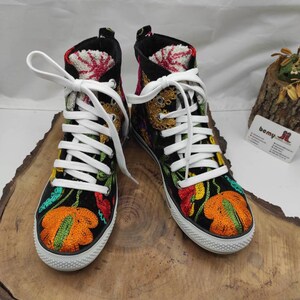 May include: A pair of black high-top sneakers with colorful floral embroidery. The sneakers have white laces and a white rubber sole.
