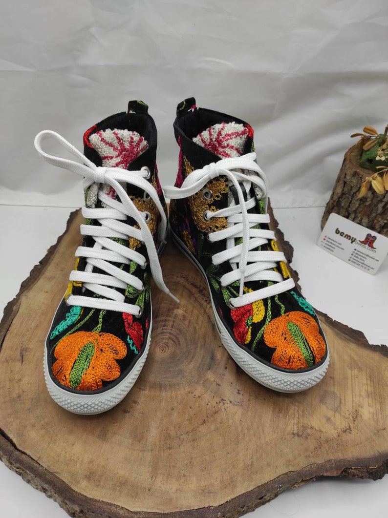 May include: A pair of black high-top sneakers with colorful floral embroidery. The sneakers have white laces and a white rubber sole.