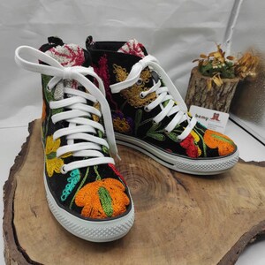 May include: Black high-top canvas shoes with colorful embroidered flowers. The shoes have white laces and a white rubber sole.
