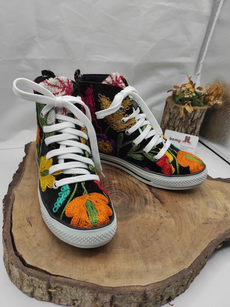 May include: Black high-top canvas shoes with colorful embroidered flowers. The shoes have white laces and a white rubber sole.