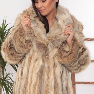 May include: A long, luxurious fur coat in shades of brown and tan. The coat features a wide collar and full sleeves. The fur appears soft and plush, offering warmth and style. The coat is a statement piece for cold weather.
