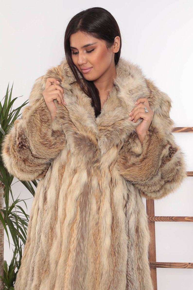 May include: A long, luxurious fur coat in shades of brown and tan. The coat features a wide collar and full sleeves. The fur appears soft and plush, offering warmth and style. The coat is a statement piece for cold weather.