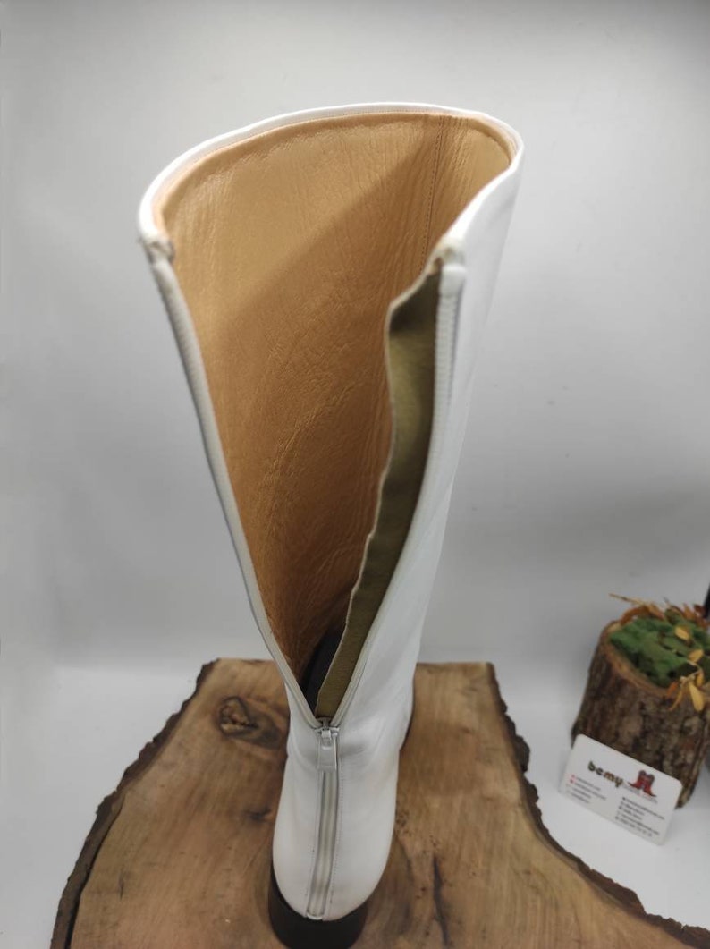 Puede incluir: Botas blancas de cuero de ca&ntilde;a alta con cremallera en la parte posterior. Las botas est&aacute;n forradas con un tejido marr&oacute;n.