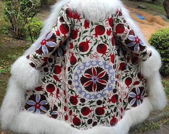 May include: A white fur-trimmed coat with a long, flowing design. The coat is embroidered with a floral pattern in red, green, and blue. The embroidery features pomegranates and other floral motifs.