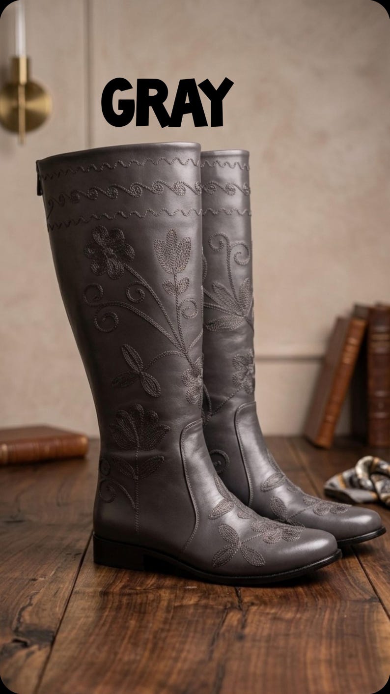 Puede incluir: Botas grises hasta la rodilla con bordados florales. Las botas tienen un patr&oacute;n decorativo cosido en la parte superior y est&aacute;n hechas de un material liso. La palabra "GRAY" est&aacute; impresa en letras negras grandes y en negrita encima de las botas.