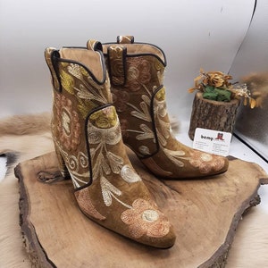 May include: A pair of brown suede ankle boots with floral embroidery. The boots have a block heel and a pointed toe.