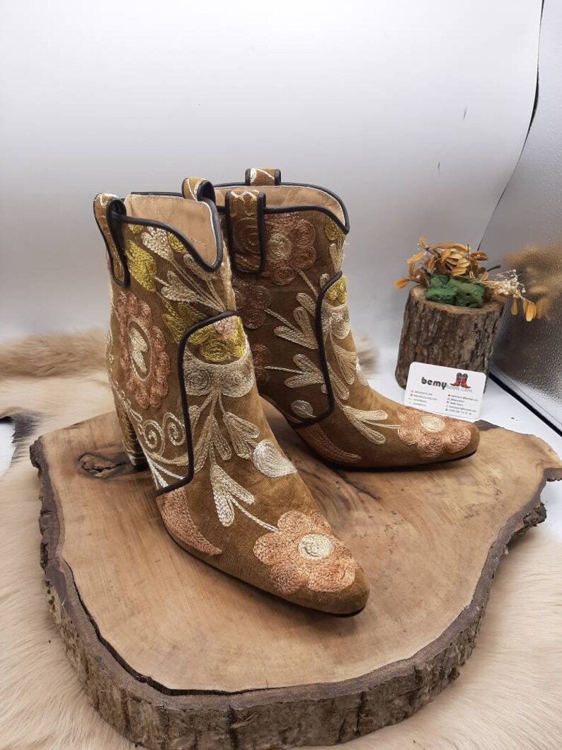 May include: A pair of brown suede ankle boots with floral embroidery. The boots have a block heel and a pointed toe.