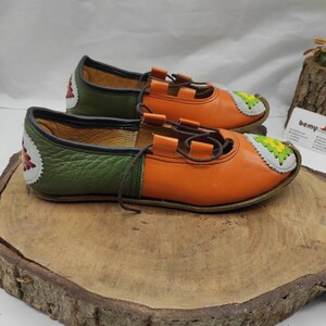 K&ouml;nnte beinhalten: Ein Paar orangefarbene und gr&uuml;ne Lederschuhe mit dekorativen N&auml;hten. Die Schuhe haben Schn&uuml;rsenkel und eine spitze Zehenpartie.