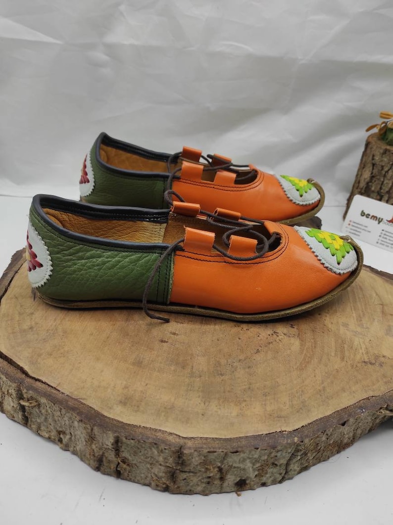 K&ouml;nnte beinhalten: Ein Paar orangefarbene und gr&uuml;ne Lederschuhe mit dekorativen N&auml;hten. Die Schuhe haben Schn&uuml;rsenkel und eine spitze Zehenpartie.