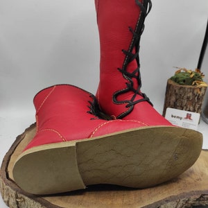 May include: A pair of red leather boots with black laces and yellow stitching. The boots have a brown leather sole with the number 40 written on it.