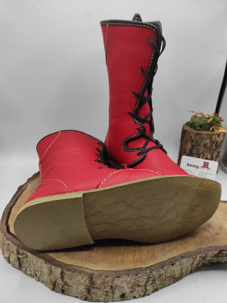 May include: A pair of red leather boots with black laces and yellow stitching. The boots have a brown leather sole with the number 40 written on it.