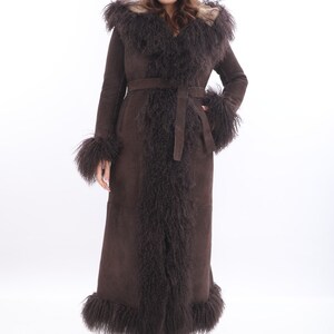 May include: A long brown suede coat with a fur collar and trim. The coat has a belt and a hood.