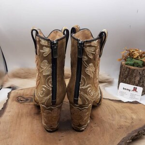 May include: A pair of brown suede ankle boots with gold embroidery and a zipper on the back. The boots have a block heel.