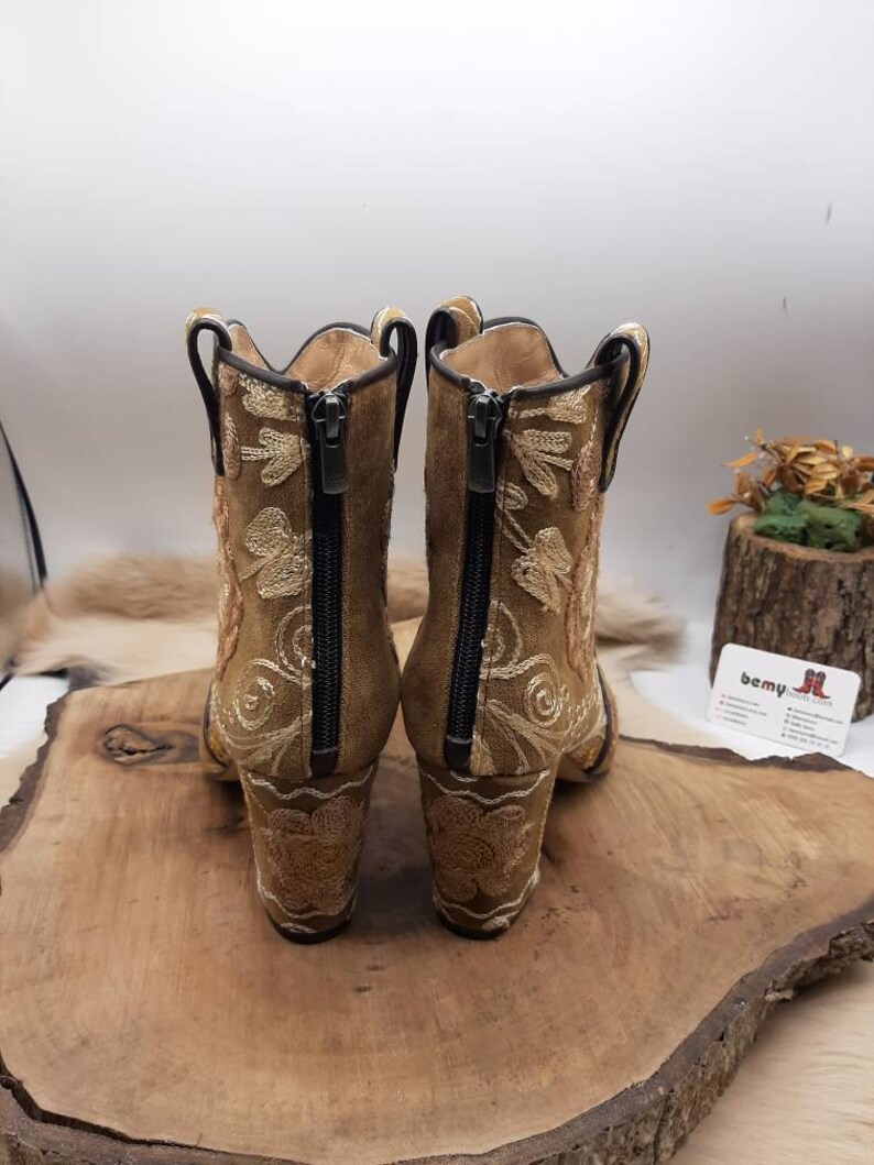 May include: A pair of brown suede ankle boots with gold embroidery and a zipper on the back. The boots have a block heel.