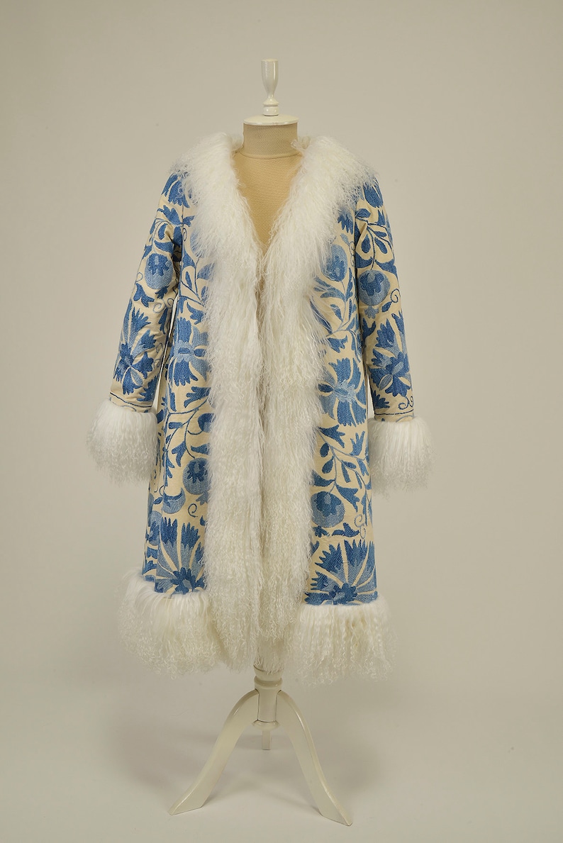 May include: A long off white fur-trimmed coat with a blue and white floral pattern. The coat is displayed on a white mannequin.