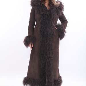 May include: A long brown suede coat with a fur trim around the hood, cuffs, and hem. The fur is a long, shaggy style and is a lighter brown color than the suede. Afgan Suede coat. Made to order.