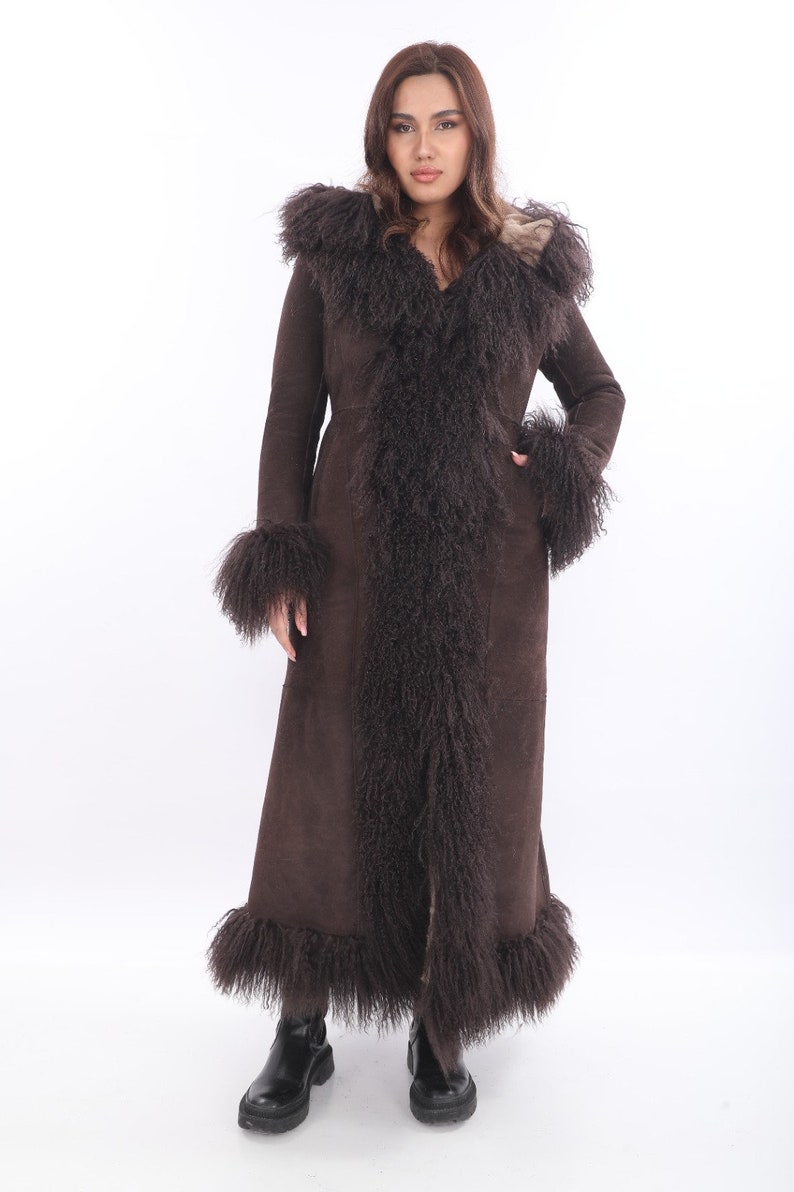 May include: A long brown suede coat with a fur trim around the hood, cuffs, and hem. The fur is a long, shaggy style and is a lighter brown color than the suede. Afgan Suede coat. Made to order.