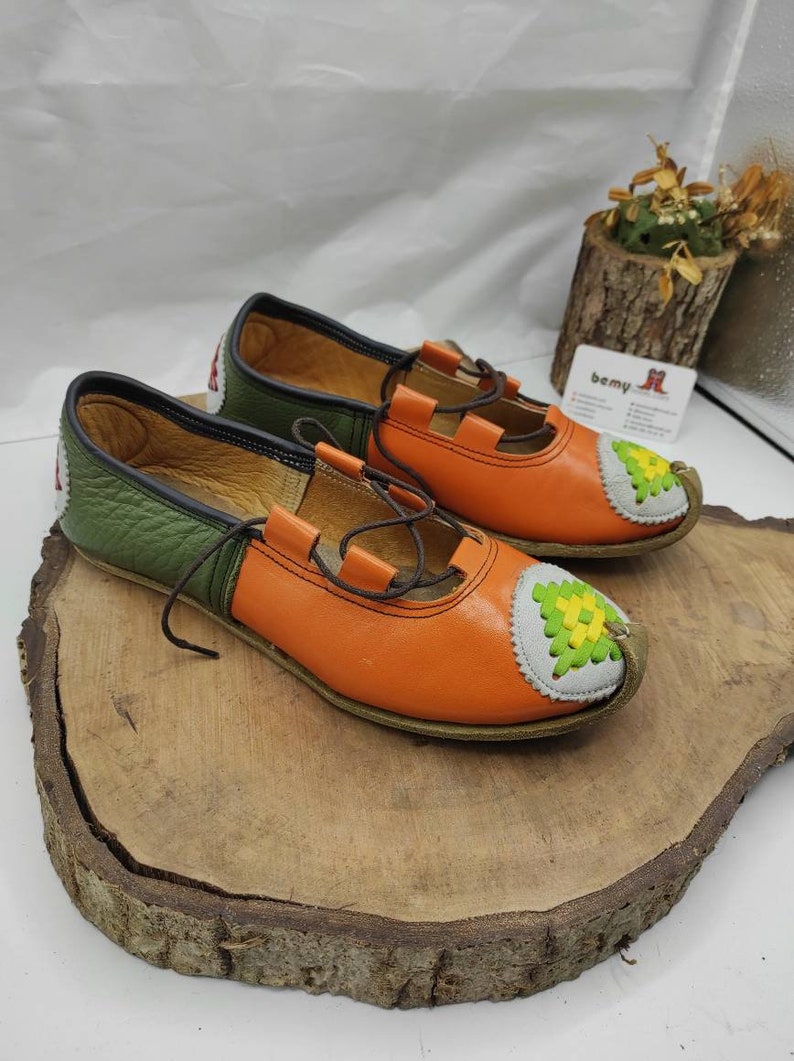 K&ouml;nnte beinhalten: Ein Paar orangefarbene und gr&uuml;ne Lederschuhe mit einem dekorativen Stichdesign an der Spitze. Die Schuhe haben einen Schn&uuml;rverschluss und eine braune Ledersohle.