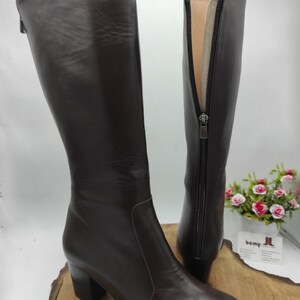May include: A pair of brown leather knee-high boots with a block heel and a zipper on the inside of the boot.