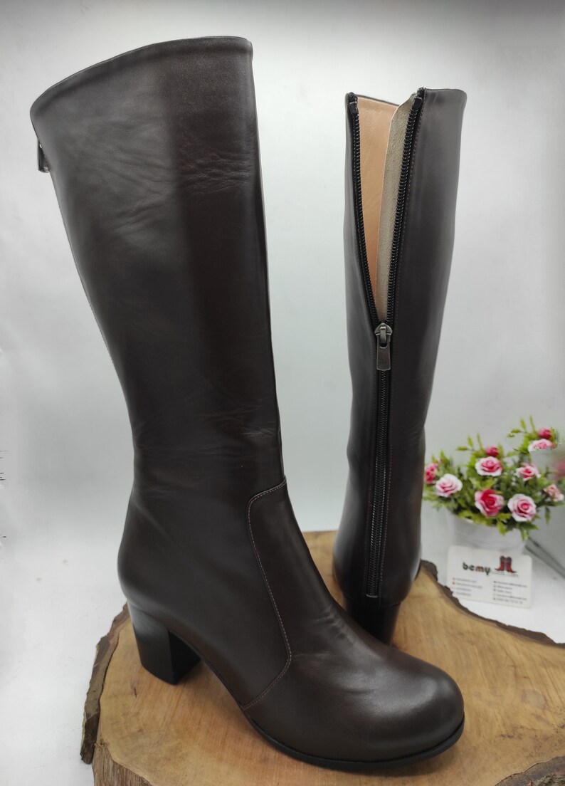 May include: A pair of brown leather knee-high boots with a block heel and a zipper on the inside of the boot.