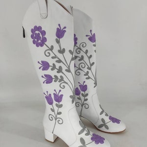 May include: White leather knee-high boots with a block heel and purple floral embroidery.