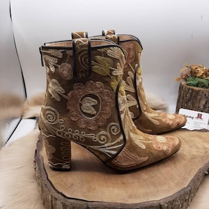 May include: A pair of brown suede ankle boots with floral embroidery. The boots have a block heel and a pointed toe.