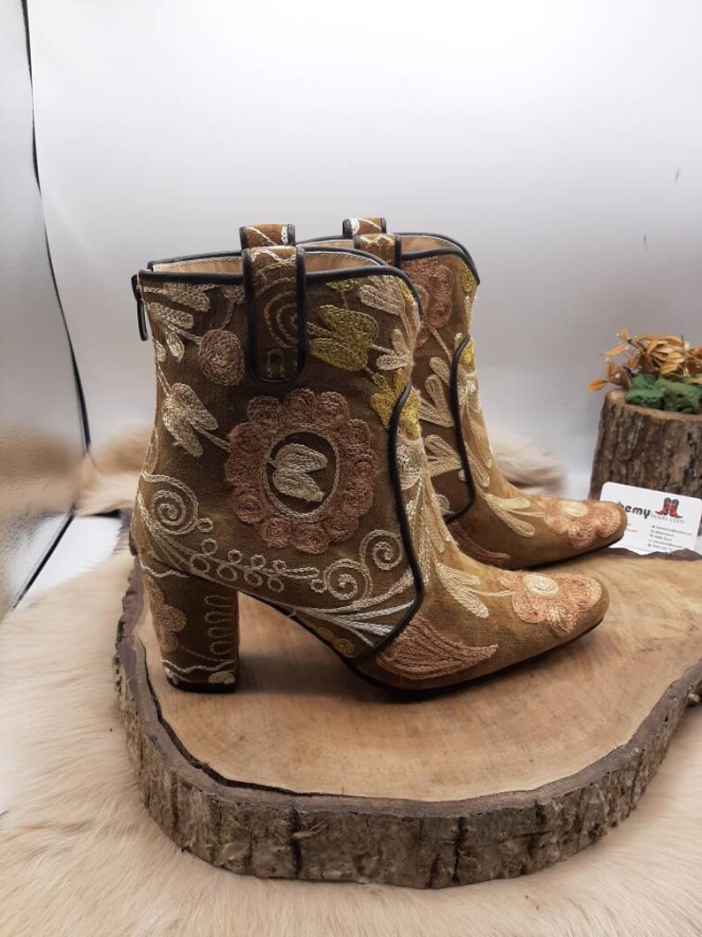 May include: A pair of brown suede ankle boots with floral embroidery. The boots have a block heel and a pointed toe.