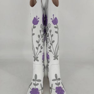 May include: White leather knee-high boots with purple and gray floral embroidery.