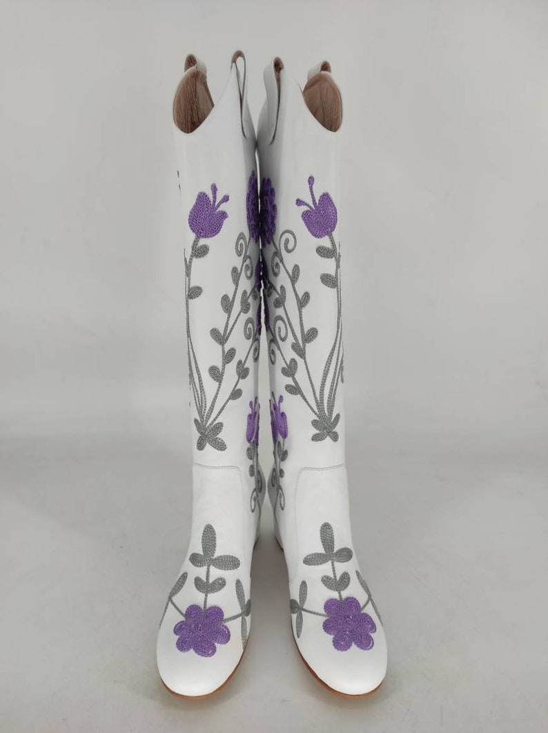 May include: White leather knee-high boots with purple and gray floral embroidery.