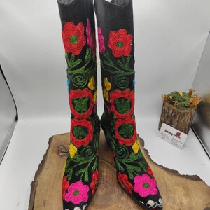 May include: A pair of black knee-high boots with colorful floral embroidery. The boots have a pointed toe and a low heel.