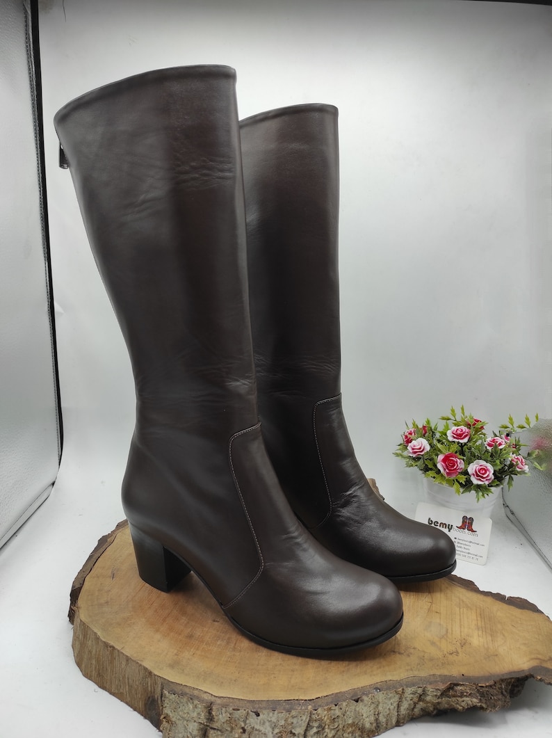 May include: A pair of brown leather knee-high boots with a block heel. The boots have a zipper on the inside of the ankle and a platform toe.