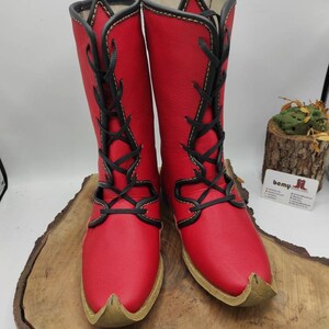 May include: A pair of red leather boots with black laces and yellow stitching. The boots have a pointed toe and are laced up the front.