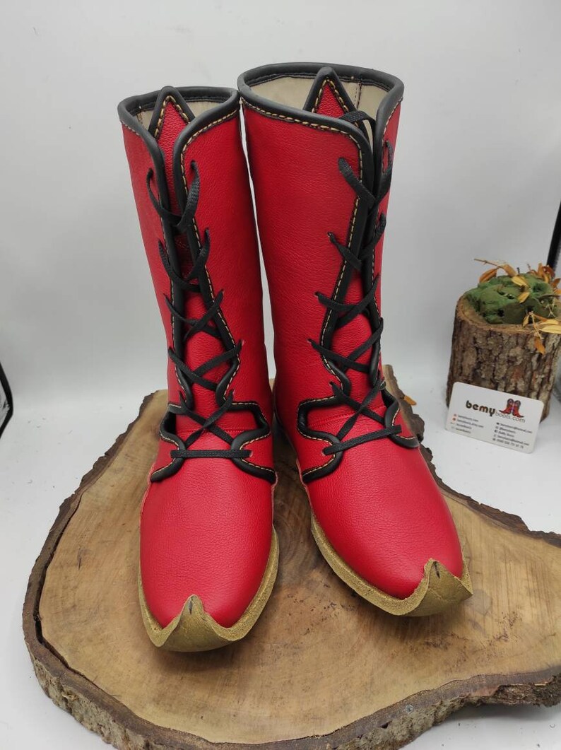 May include: A pair of red leather boots with black laces and yellow stitching. The boots have a pointed toe and are laced up the front.