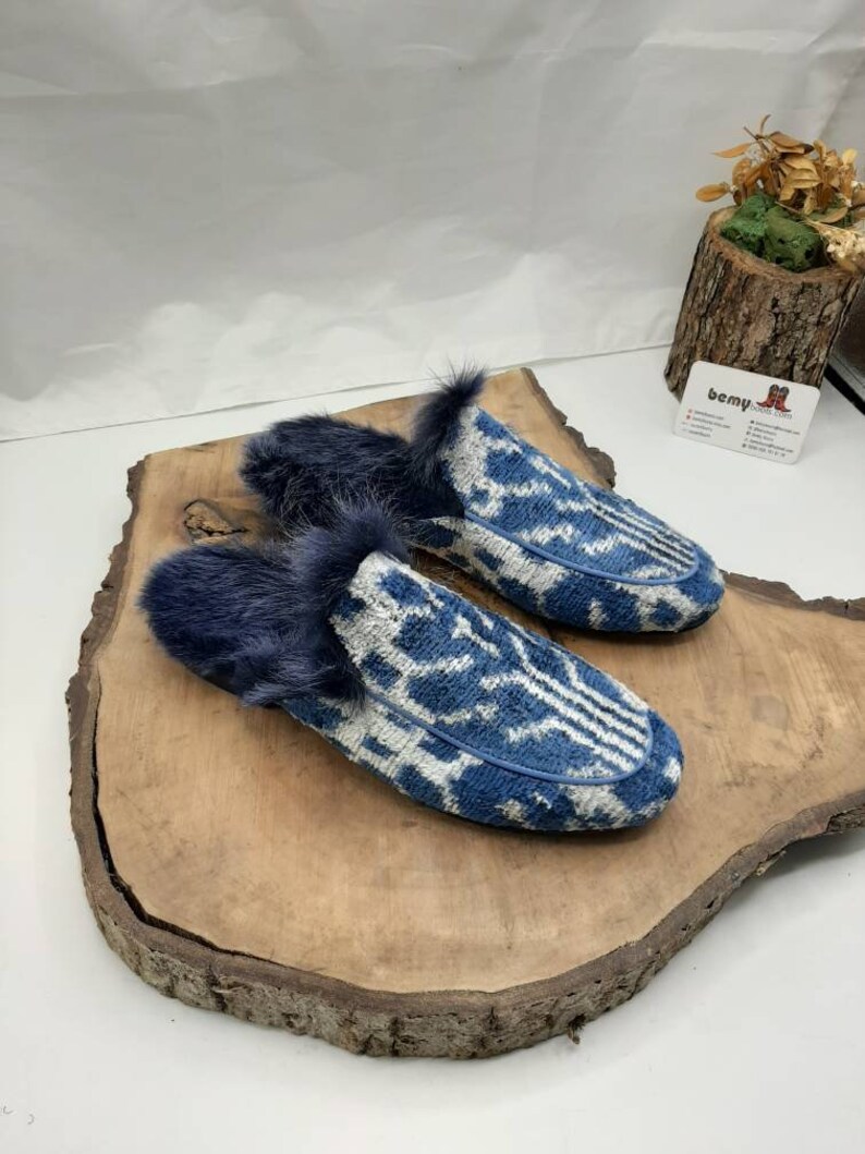 May include: A pair of blue and white patterned slippers with a fuzzy blue lining. The slippers are on a wooden surface.
