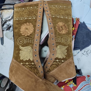 May include: A pair of brown leather boots with gold embroidery and eyelets. The boots have a pointed toe and a low heel.