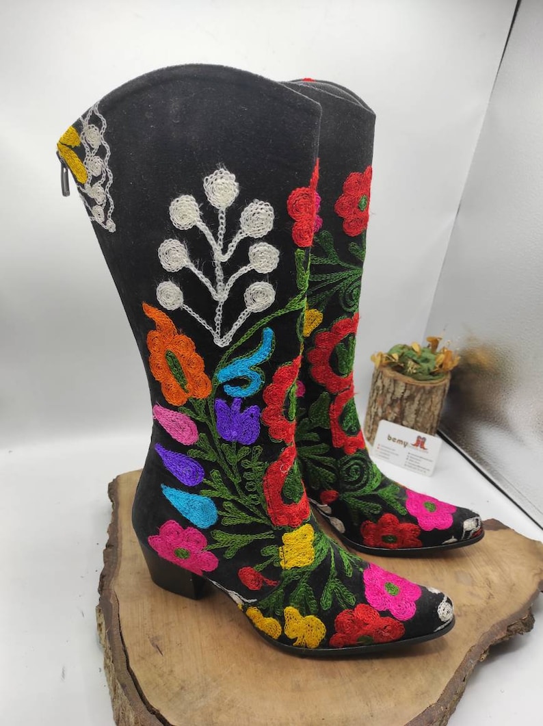 May include: Black suede boots with colorful floral embroidery. The boots have a pointed toe and a block heel.
