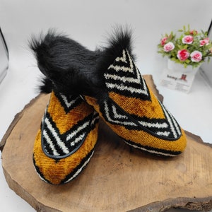 Puede incluir: Un par de zapatillas de terciopelo amarillo mostaza con patrones geom&eacute;tricos en blanco y negro. Las zapatillas tienen un ribete de piel sint&eacute;tica negra alrededor de la parte superior.