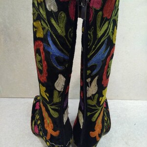 May include: A pair of black knee-high boots with colorful floral embroidery. The boots have a zipper on the back and a block heel.