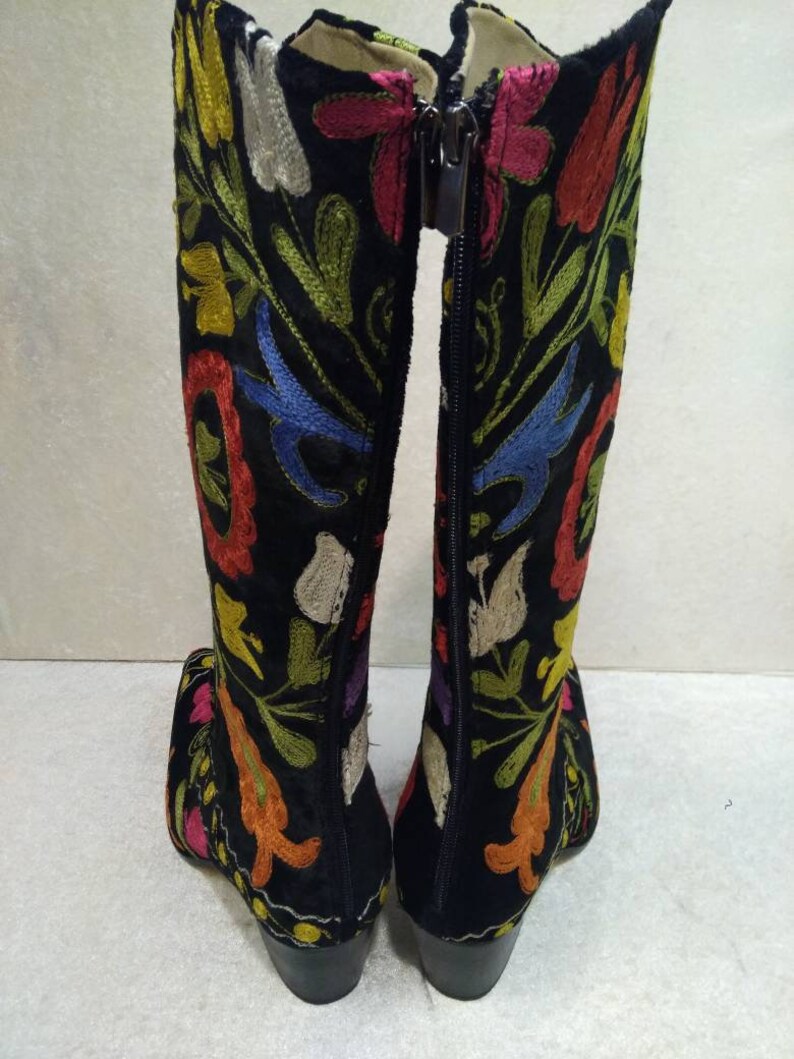May include: A pair of black knee-high boots with colorful floral embroidery. The boots have a zipper on the back and a block heel.