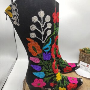 May include: Black suede boots with colorful floral embroidery. The boots have a pointed toe and a block heel.